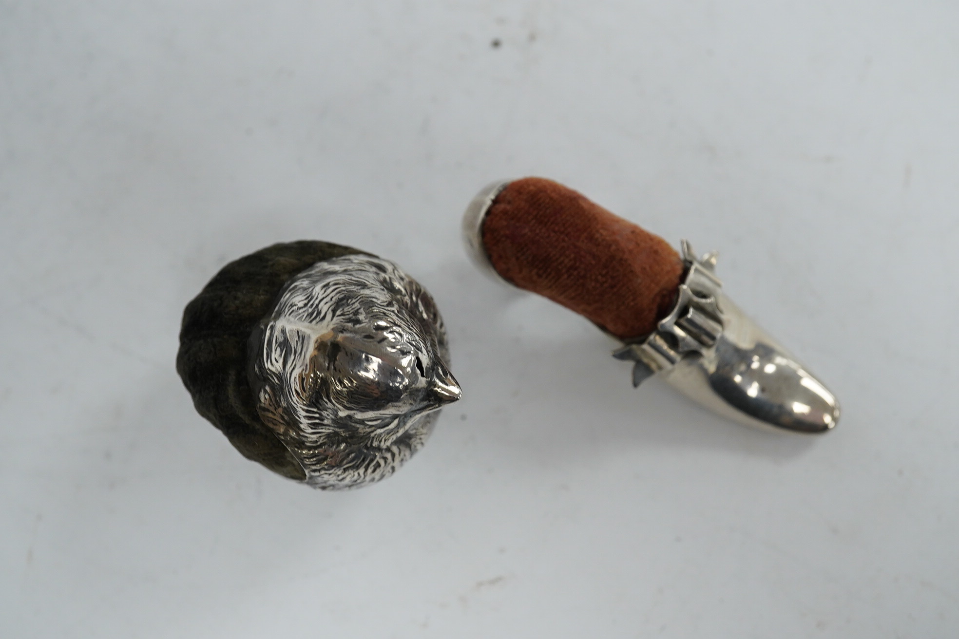 An Edwardian novelty silver pin cushion, modelled as a hatching chick, by Sampson Mordan & Co, Sheffield, 1906, height 43mm (hole), together with a late Victorian shoe pin cushion, by Adie & Lovekin, Birmingham, 1892, Co